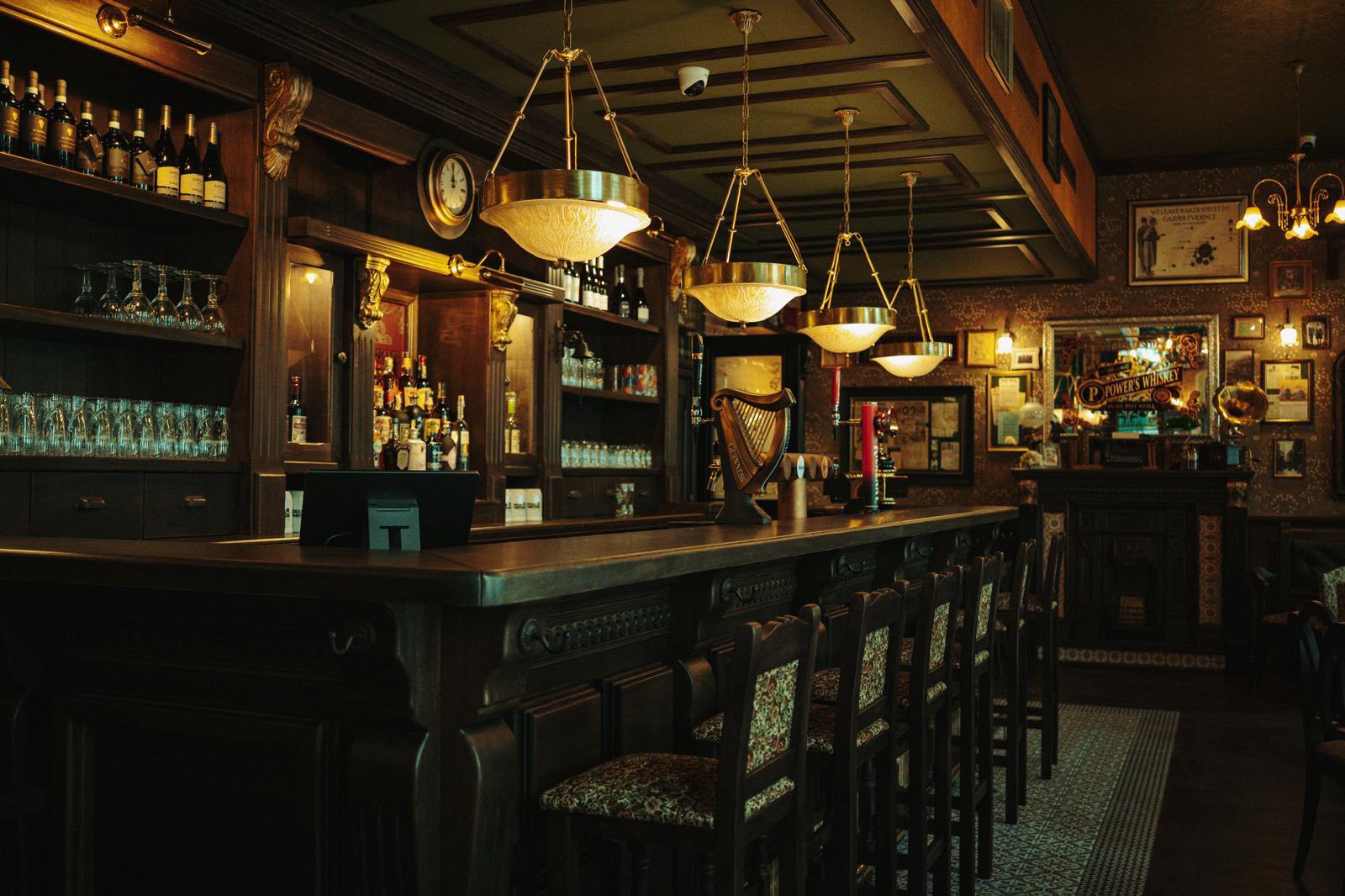 Dear Watson bar with dark wood, brass lights, bottle shelves, and a Guinness harp.
