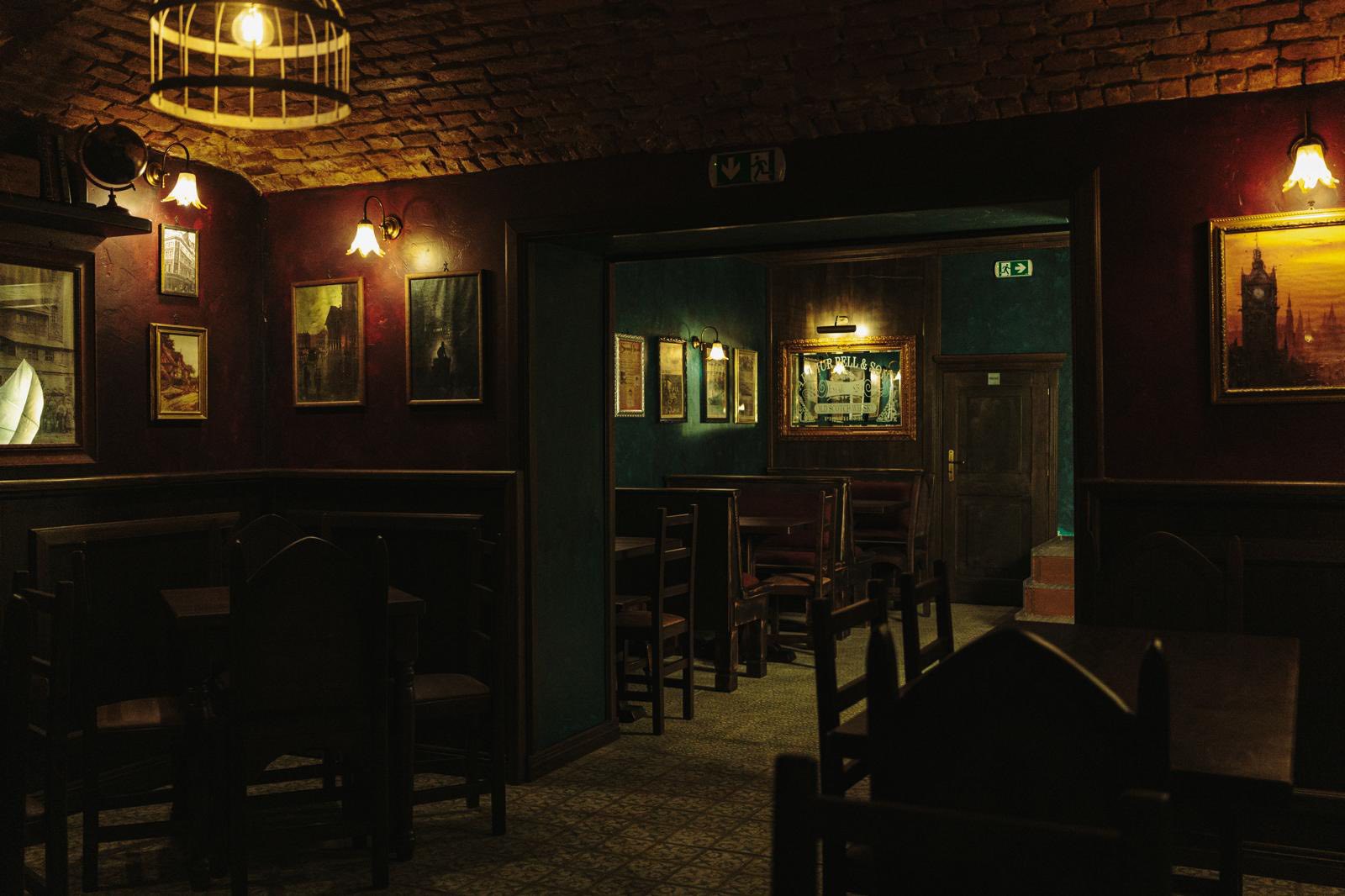 Warm Dear Watson back room with patterned wallpaper, framed art, and pub tables.