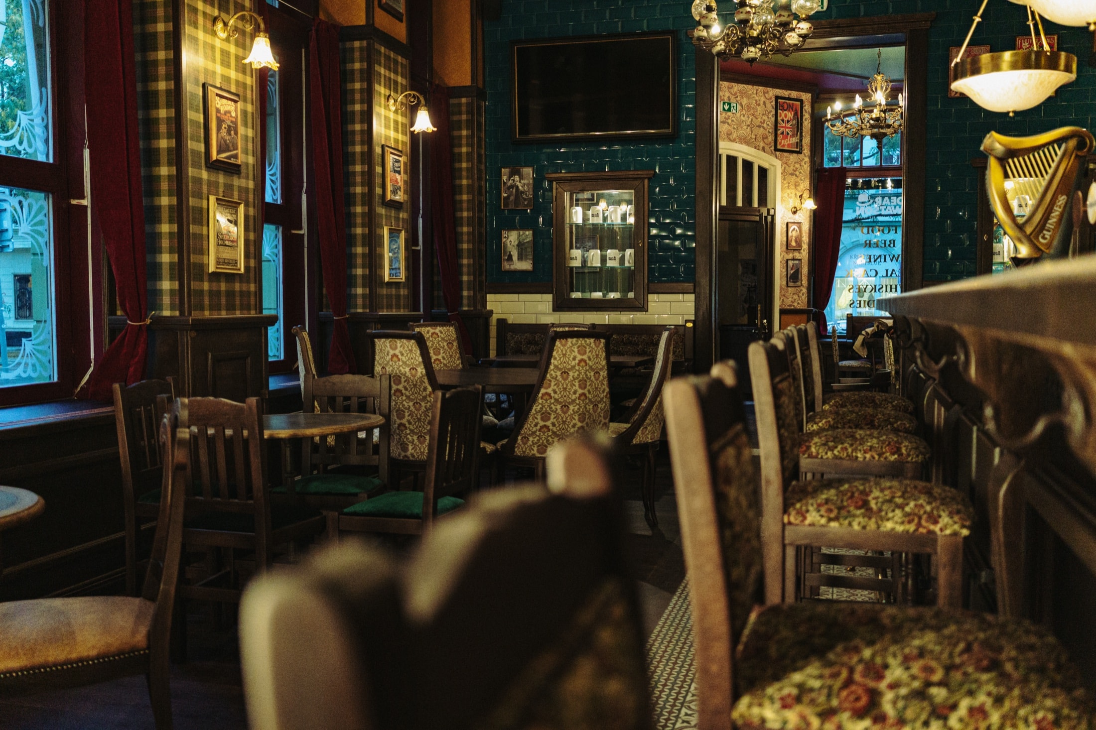 Dear Watson dining room with patterned chairs, green tile, brass lamps, and dark wood tables.