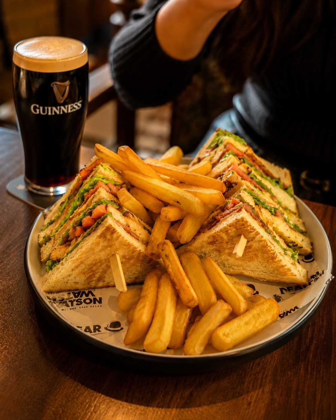 Dear Watson sandwich with chips on a plate lined with branded paper.